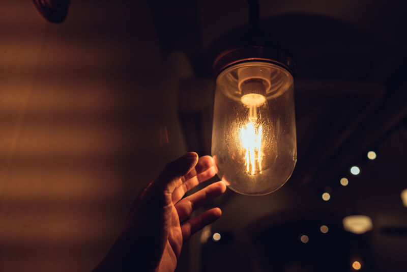 Imagem de uma mão encostando em uma lâmpada acesa.